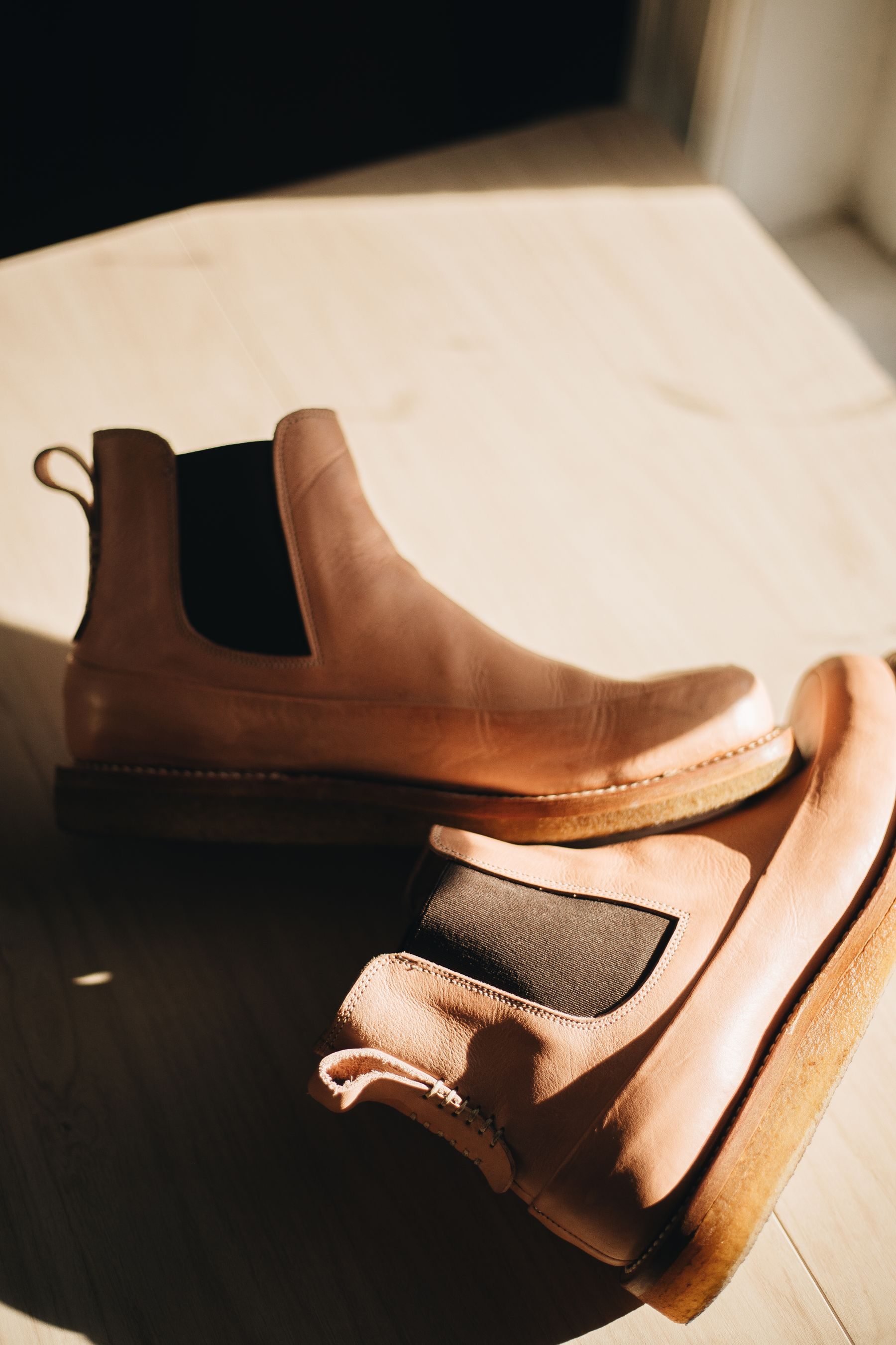 A pair of tan leather Chelsea boots in warm light on a pale floor
